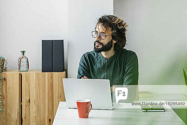 Thoughtful freelancer sitting with laptop at desk