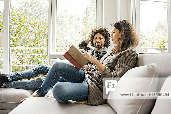 Man with woman reading book on sofa at home