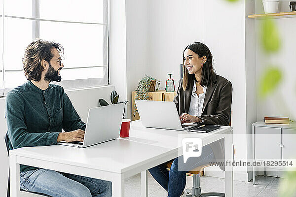 Happy business colleagues discussing with laptop at desk in workplace