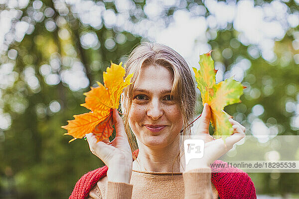 Smiling young woman holding maple leaves at park