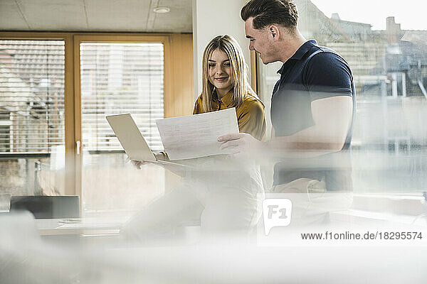 Smiling young businesswoman discussing over document with colleague in office