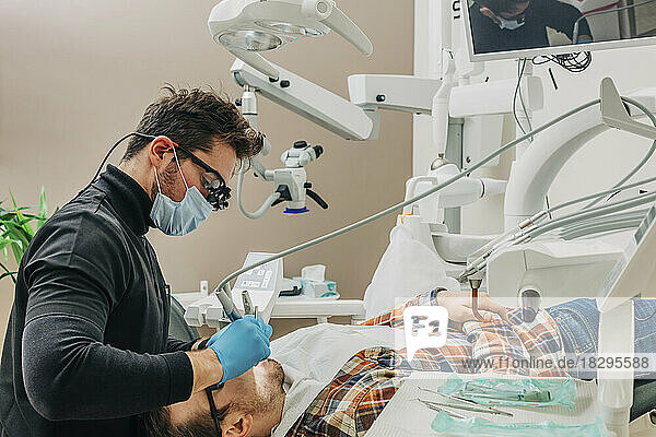 Junger Zahnarzt untersucht die Zähne des Patienten mit Geräten in der Klinik
