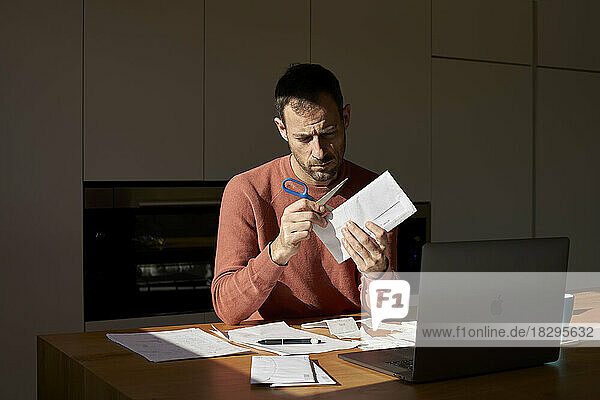 Man opening envelope with scissors at home