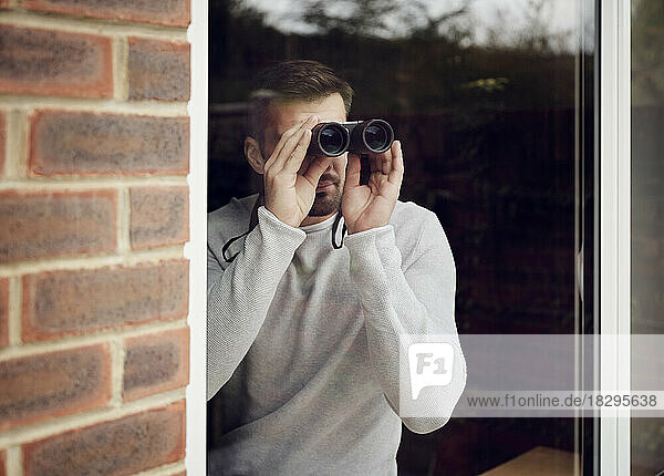 Mann schaut zu Hause mit Fernglas aus dem Fenster