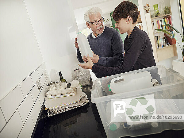 Grandfather and grandson putting separated waste into recycling box