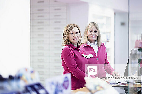 Smiling pharmacist standing with colleague at desk
