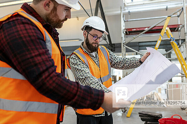 Engineer discussing over blueprint with colleague at construction site