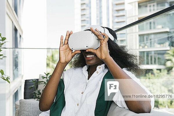 Happy woman wearing virtual reality simulators sitting on balcony