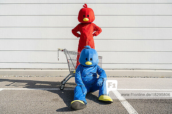 Friends wearing red and blue costumes with shopping cart in front of white wall