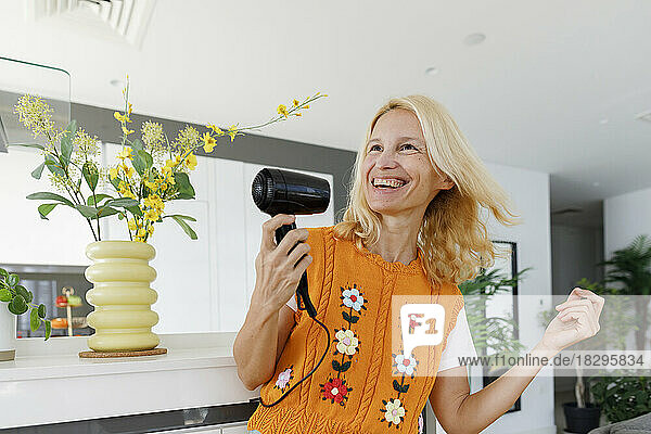 Cheerful woman dancing with hairdryer at home