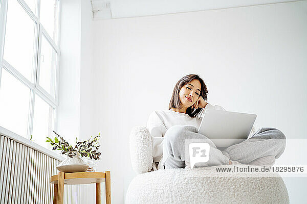 Young woman using laptop sitting on chair at home