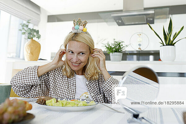 Happy woman wearing crown headband sitting at dining table