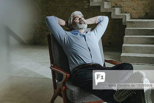 Mature architect relaxing in chair with hands behind head at under construction site