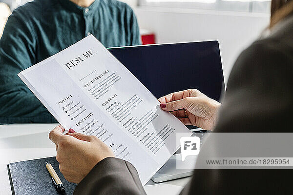 Hands of recruiter holding resume in front of candidate at desk