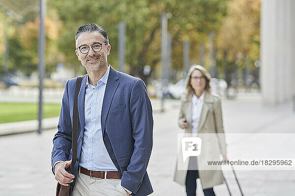 Smiling mature businessman with businesswoman in background on footpath