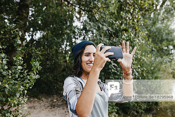 Smiling young woman clicking photos using smart phone in park