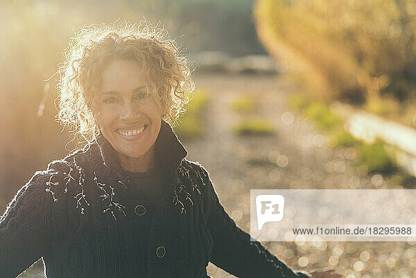 Glückliche reife Frau mit lockigem Haar an einem sonnigen Tag