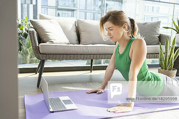 Woman doing online yoga class using laptop on balcony