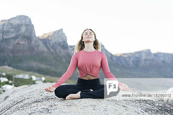 Young woman meditating on rock at beach