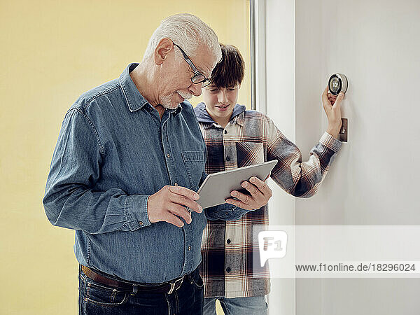 Grandfather and grandson looking at smart thermostat control on digital tablet at home