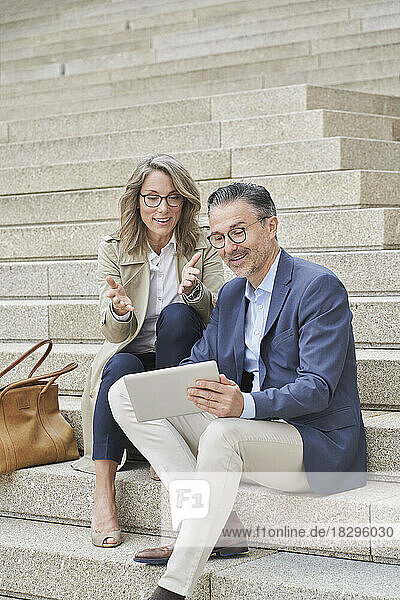 Smiling business colleagues discussing over tablet PC on steps