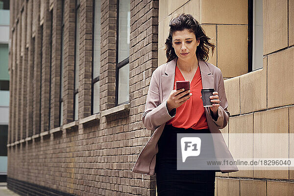 Businesswoman using smart phone by building