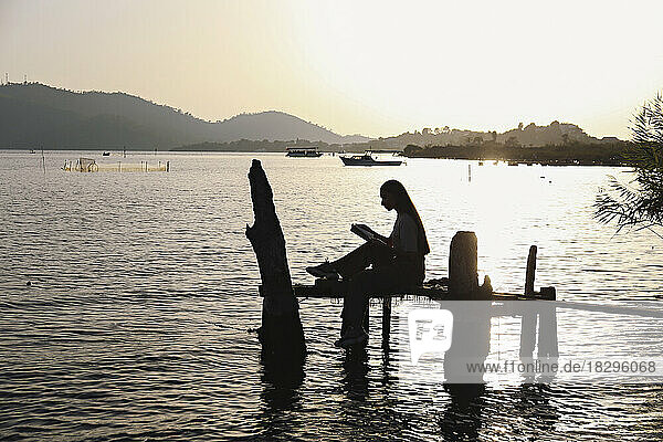 Silhouette young woman sitting on handmade fishing platform in sea