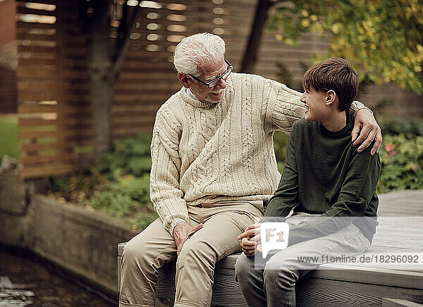 Enkel und Großvater sitzen im Garten und reden miteinander