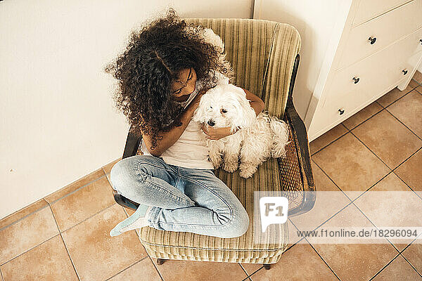 Girl sitting with dog on chair at home