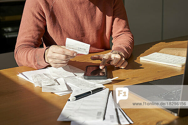 Hände eines Mannes mit Finanzrechnungen  die auf dem Smartphone am Schreibtisch rechnen