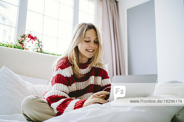 Happy girl using laptop on bed at home