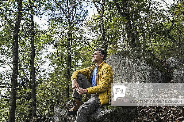 Contemplative man with backpack sitting on rock in forest
