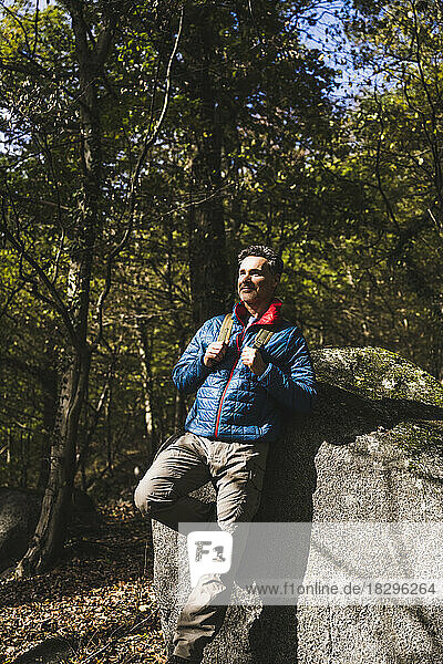 Mature man leaning on rock in forest on sunny day