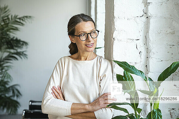Smiling businesswoman with arms crossed leaning on wall in office