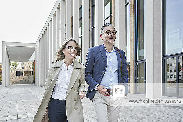Happy business colleagues walking by building on footpath