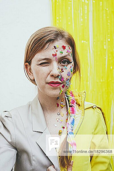 Woman with stickers on face winking in front of two tone wall