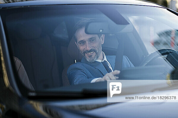 Smiling mature businessman checking GPS seen through windshield of car