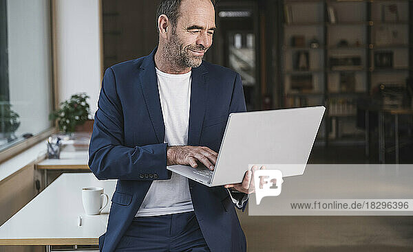 Lächelnder reifer Geschäftsmann  der im Büro am Laptop arbeitet