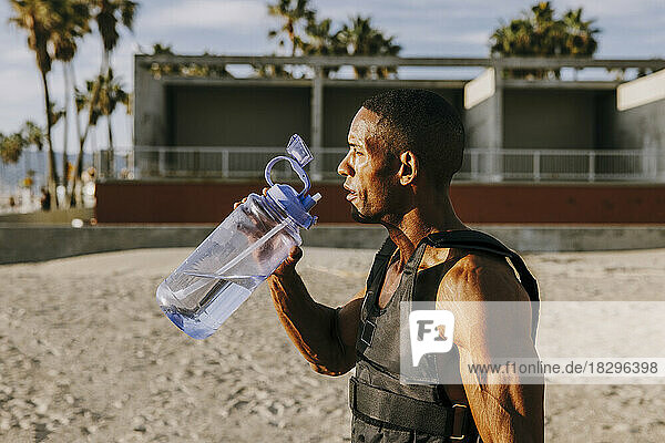 Thirsty sportsman standing with water bottle at beach