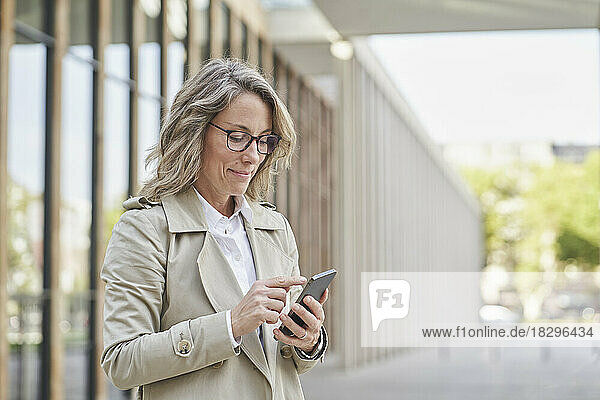 Mature businesswoman using mobile phone standing outside building