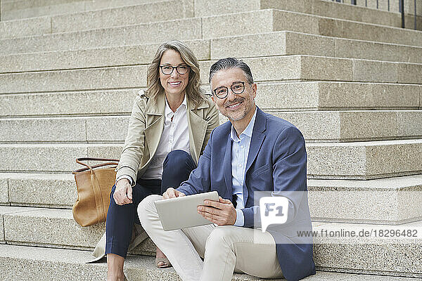 Lächelnde reife Geschäftsleute mit Tablet-PC sitzen auf Stufen