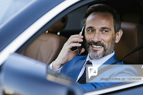 Lächelnder Geschäftsmann  der im Auto sitzt und über sein Smartphone spricht
