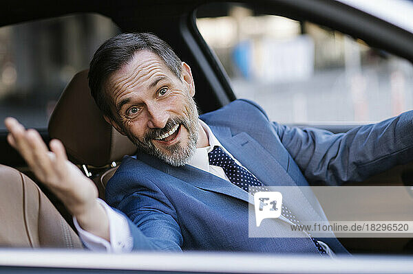 Happy mature businessman gesturing sitting on driver's seat in car