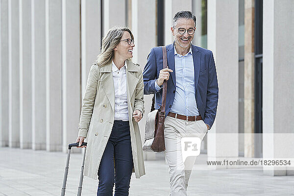 Happy mature businesswoman walking with colleague on footpath