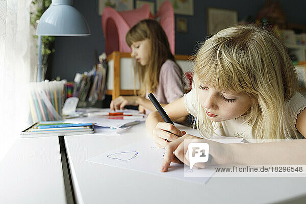 Girl with sister drawing on paper at desk