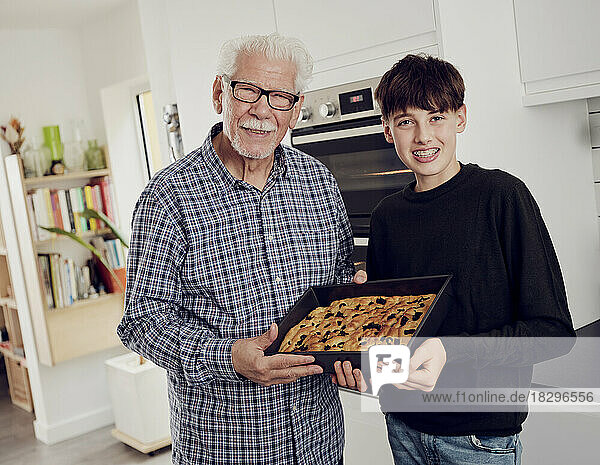 Portrait of grandfather and grandson holding baking tray with fresh focaccia bread in the kitchen