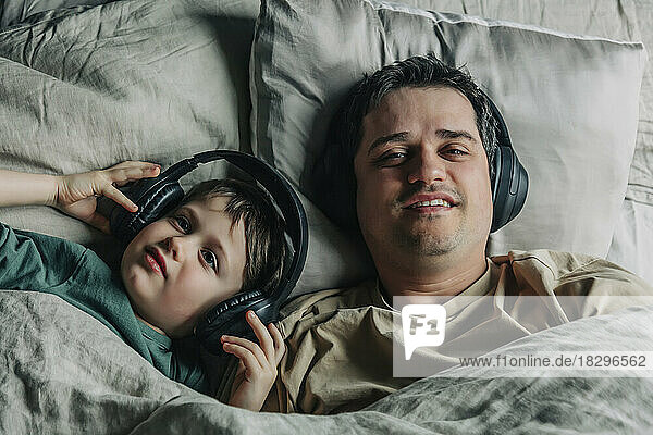 Vater und Sohn tragen Kopfhörer und hören Musik im Bett