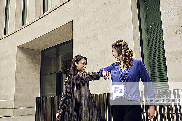 Happy young businesswoman elbow bumping with colleague in front of building