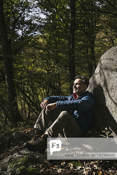 Contemplative man sitting by rock in forest