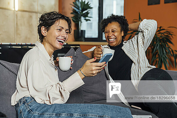 Fröhliche Geschäftsfrau benutzt Smartphone auf dem Sofa im Büro